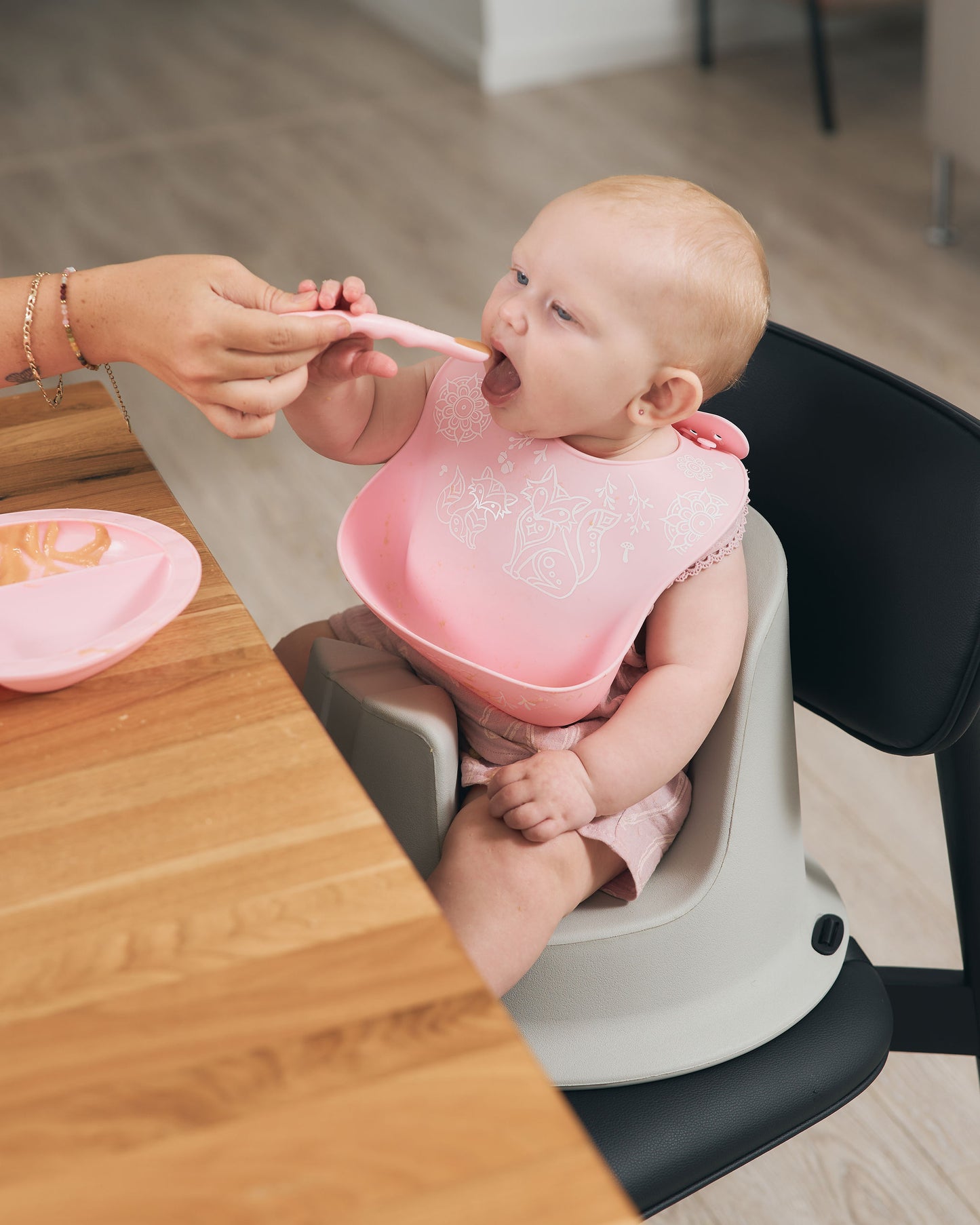 Baby in the Hip & Co floor seat used as a booster, enjoying a bite of food at the table.