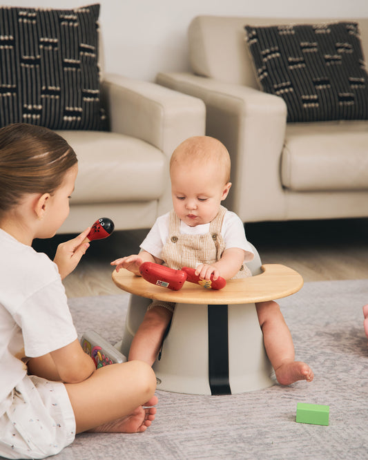 Baby supported in the Hip & Co floor seat, smiling and playing with their sibling.