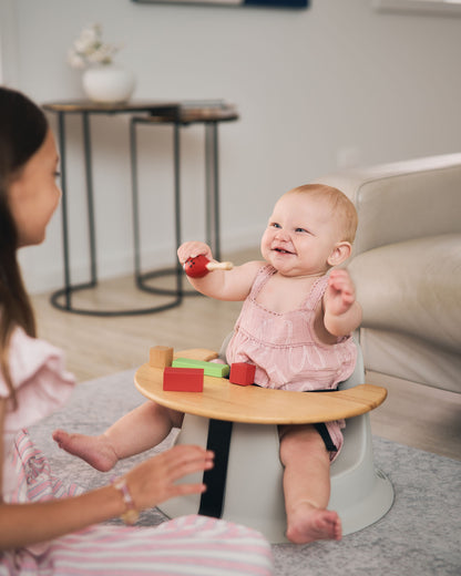Baby in the Hip & Co floor seat laughing and interacting with an older child.
